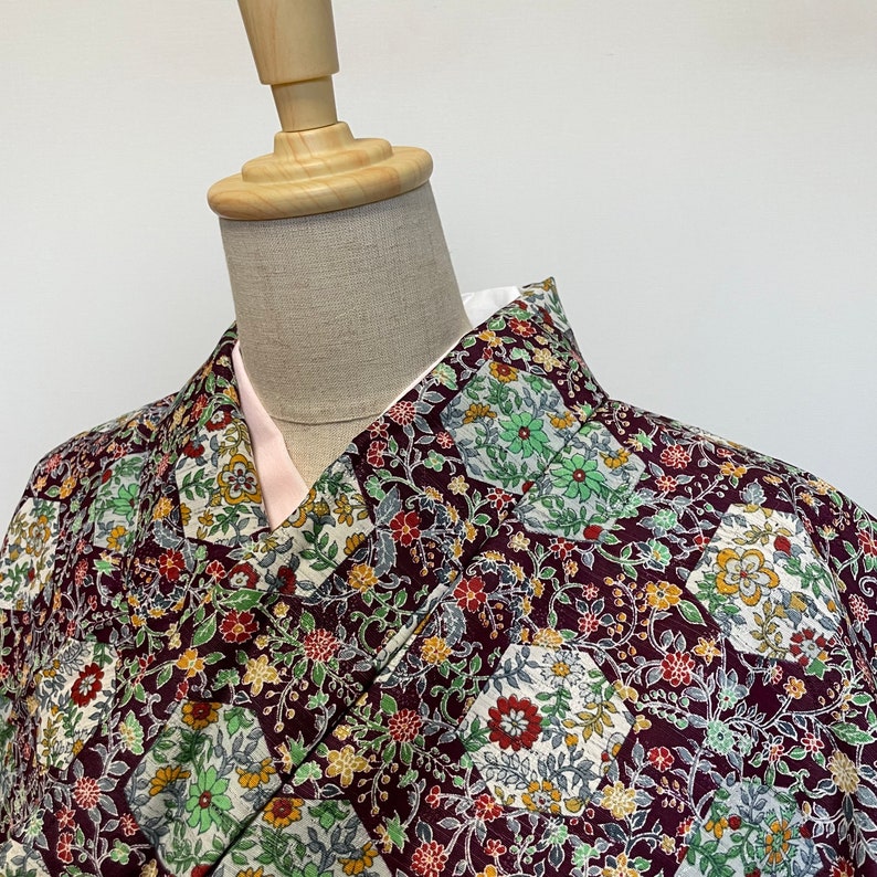May include: A burgundy kimono with a floral pattern featuring green, white, and yellow accents. The kimono is made of a soft, lightweight fabric and has a traditional Japanese design.