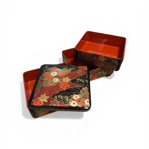 Pode incluir: Uma caneca de cerâmica branca com uma alça preta e o texto "But First, Coffee" em negrito preto. A caneca está sobre um fundo desfocado, sugerindo um ambiente acolhedor.