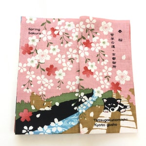Op de afbeelding: Een roze stoffen paneel met een kersenbloesem patroon en twee zwarte honden. Het paneel heeft de tekst "Spring Sakura" en "Tetsugakunomichi Kyoto gosho" in zwart. Het paneel heeft ook de tekst "春桜" en "哲学の道・京都御所" in het Japans.