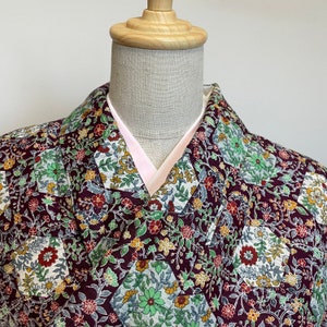 May include: A maroon kimono with a floral pattern in shades of green, white, and yellow. The kimono has a pink lining and a traditional collar.