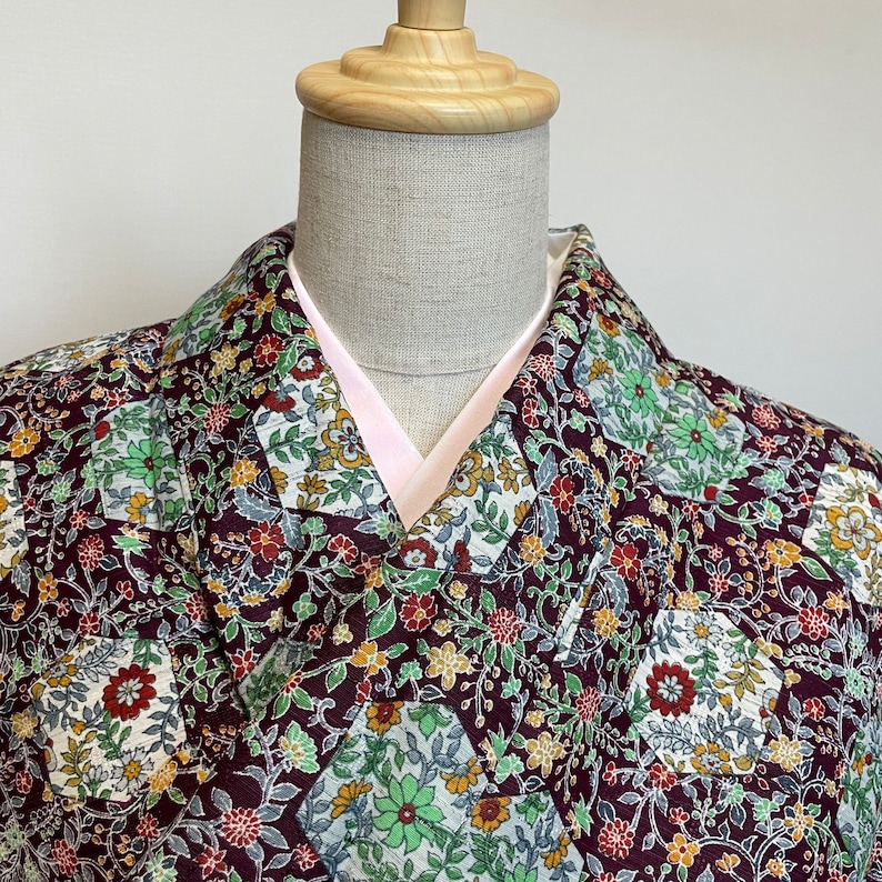 May include: A maroon kimono with a floral pattern in shades of green, white, and yellow. The kimono has a pink lining and a traditional collar.