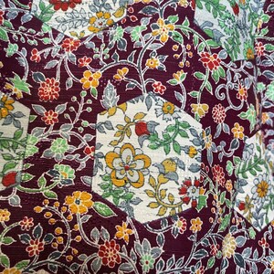 May include: A close-up of a fabric with a repeating pattern of flowers and leaves. The fabric is a dark purple color with white, yellow, and green accents. The pattern is made up of small, intricate details.