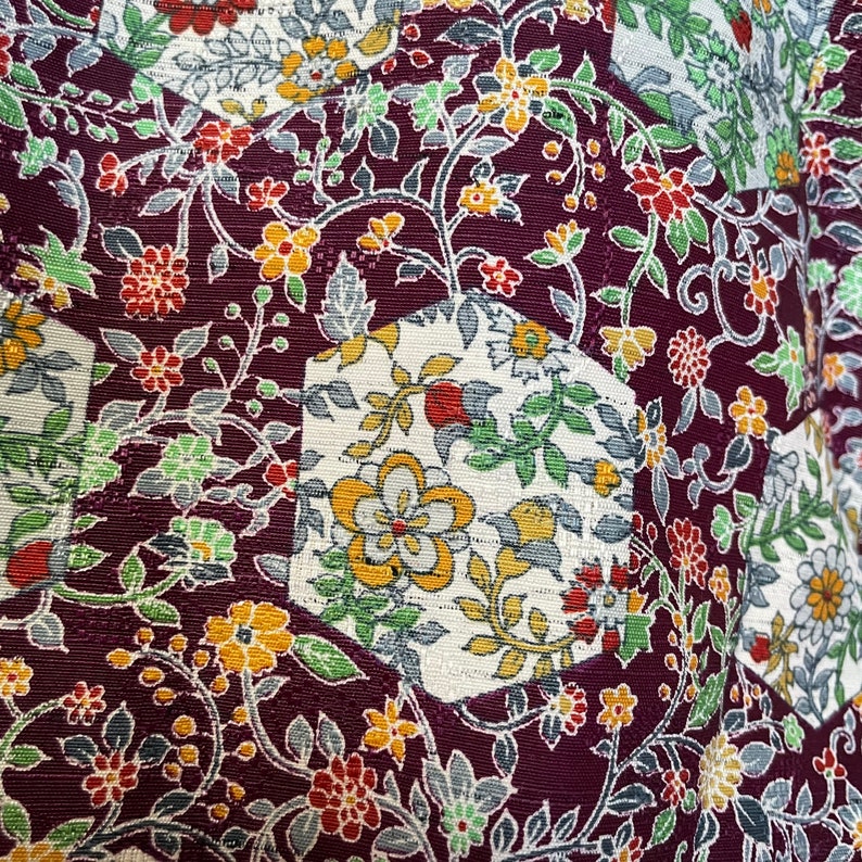 May include: A close-up of a fabric with a repeating pattern of flowers and leaves. The fabric is a dark purple color with white, yellow, and green accents. The pattern is made up of small, intricate details.