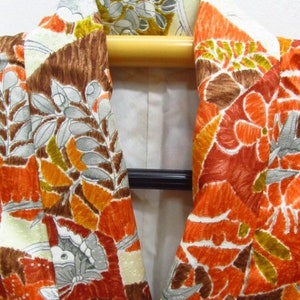 Puede incluir: Primer plano del cuello de un kimono marr&oacute;n, naranja y blanco con un patr&oacute;n floral. El kimono est&aacute; en una percha de madera.