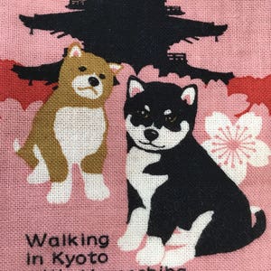 Op de afbeelding: Een roze stoffen tas met een zwart-witte illustratie van twee Shiba Inu honden. De honden lopen voor een zwarte silhouet van een pagode met roze kersenbloesems. De tekst "Walking in Kyoto with Mameshiba" staat op de tas gedrukt.