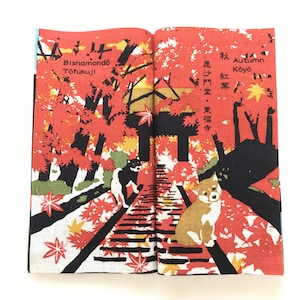 Op de afbeelding: Een open boek met een rode en zwarte illustratie van een pad door een bos met rode en gele bladeren. De tekst op het boek luidt "Autumn Koyo" en "Bishamondo Tofukuji".