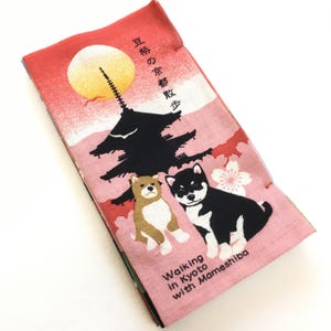 Op de afbeelding: Een roze en rode stoffen tas met een Japanse pagode, kersenbloesems en twee Shiba Inu honden. De tekst op de tas luidt "Vroege lente-excursie" in het Japans en "Wandelen in Kyoto met Mameshiba" in het Engels.