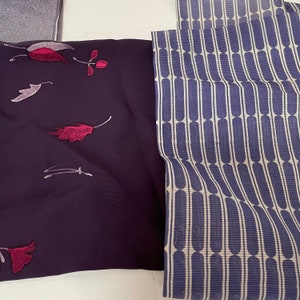 May include: Two fabric swatches, one with a dark purple background and a floral pattern in shades of pink and white, and the other with a white background and a blue and white striped pattern.