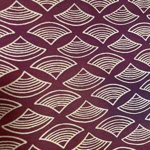 May include: A close-up of a fabric with a repeating pattern of white stylized waves on a deep burgundy background.
