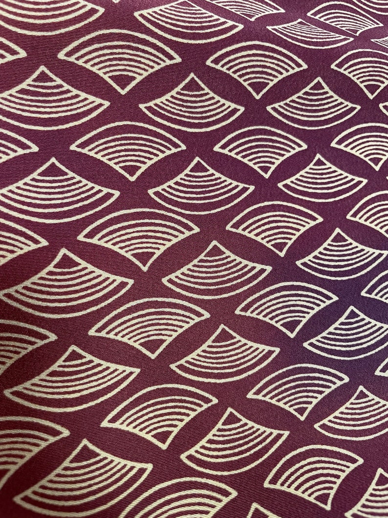 May include: A close-up of a fabric with a repeating pattern of white stylized waves on a deep burgundy background.