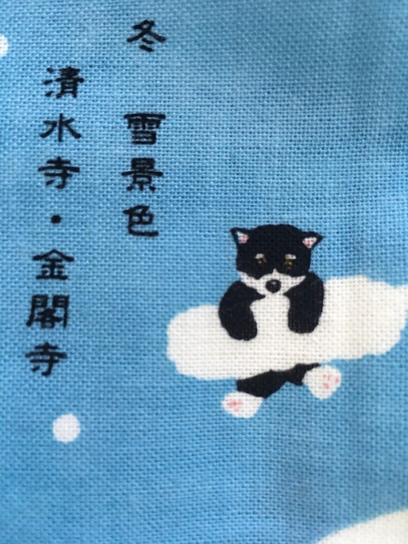Op de afbeelding: Een blauwe stof met witte wolken en een zwart-witte pandabeer die op een wolk zit. De stof heeft Japanse tekst die "Winter, helder water, gouden haan" luidt.