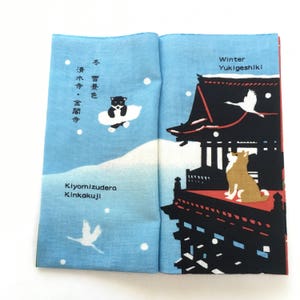 Op de afbeelding: Een blauw en wit stoffen paneel met een Japanse wintersc&egrave;ne. Het paneel toont een zwart-witte hond, een kraanvogel en een tempel met de tekst "Winter Yukigeshiki" en "Kiyomizudera Kinkakuji".