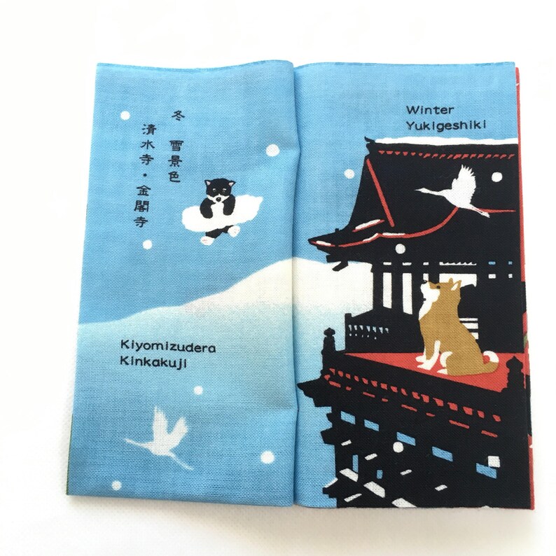 Op de afbeelding: Een blauw en wit stoffen paneel met een Japanse wintersc&egrave;ne. Het paneel toont een zwart-witte hond, een kraanvogel en een tempel met de tekst "Winter Yukigeshiki" en "Kiyomizudera Kinkakuji".