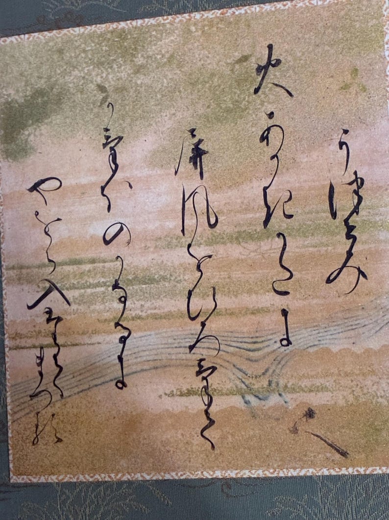 May include: Close-up of a traditional Japanese artwork featuring calligraphy in black ink on a beige and green background. The artwork has a textured appearance and is framed with a patterned border.