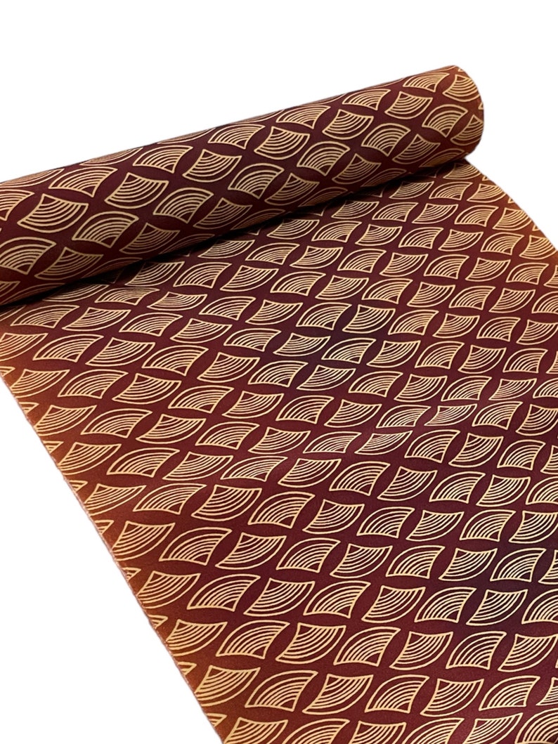 May include: A roll of fabric with a repeating pattern of gold geometric shapes on a burgundy background.