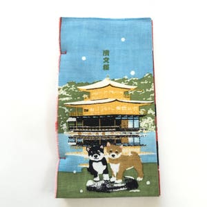 Op de afbeelding: Een blauw en groen stoffen paneel met een Japanse tempel en twee honden. De tempel is goud en heeft een rood dak. De honden zijn zwart-wit en bruin. De tekst op het paneel luidt "清水寺".