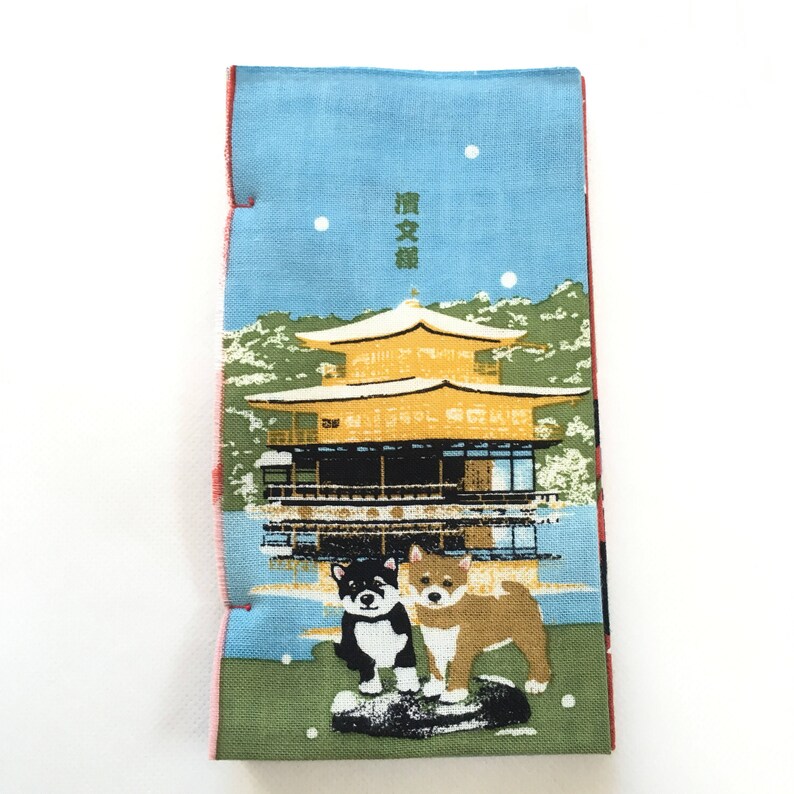 Op de afbeelding: Een blauw en groen stoffen paneel met een Japanse tempel en twee honden. De tempel is goud en heeft een rood dak. De honden zijn zwart-wit en bruin. De tekst op het paneel luidt "清水寺".