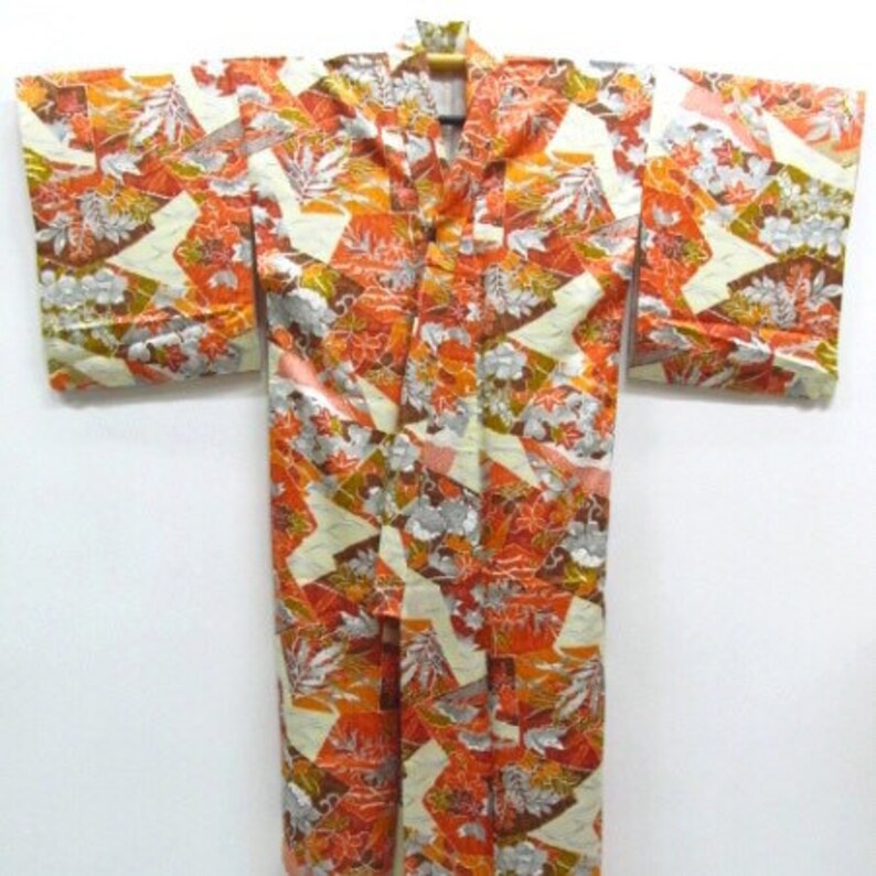 Puede incluir: Un kimono japon&eacute;s tradicional con fondo blanco y un patr&oacute;n geom&eacute;trico colorido de naranja, marr&oacute;n y plateado. El kimono tiene una silueta larga y fluida y es perfecto para ocasiones especiales.