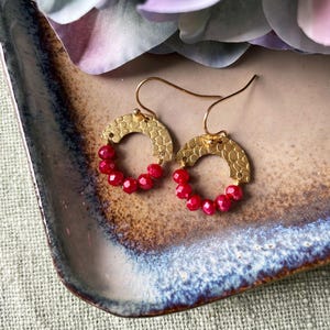May include: Gold hoop earrings with a hammered texture and a row of bright red beads around the bottom half of the hoop.