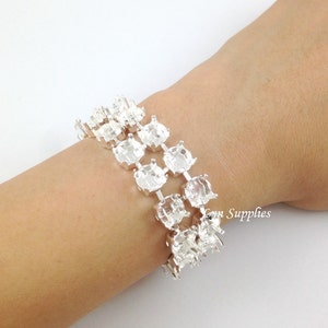 May include: Silver bracelet with multiple rows of round settings for rhinestones. The bracelet is shown on a person's wrist.