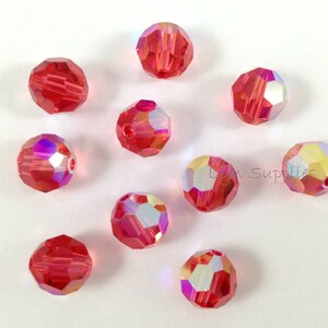May include: Ten red crystal beads with iridescent facets. The beads are round and have a faceted design.