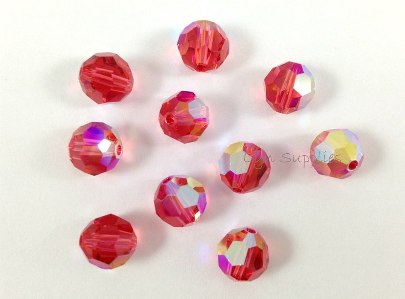 May include: Ten red crystal beads with iridescent facets. The beads are round and have a faceted design.