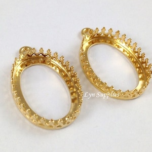 May include: Two gold-tone oval-shaped pendant settings with a crown-like border. The settings are designed to hold a cameo or other decorative element.