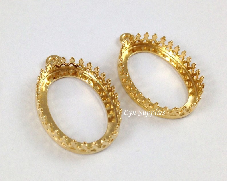 May include: Two gold-tone oval-shaped pendant settings with a crown-like border. The settings are designed to hold a cameo or other decorative element.