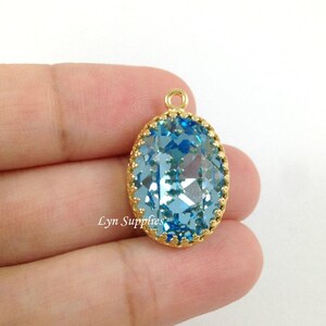May include: A gold-toned pendant with a large, oval-shaped, light blue crystal. The crystal is faceted and has a gold-toned border.