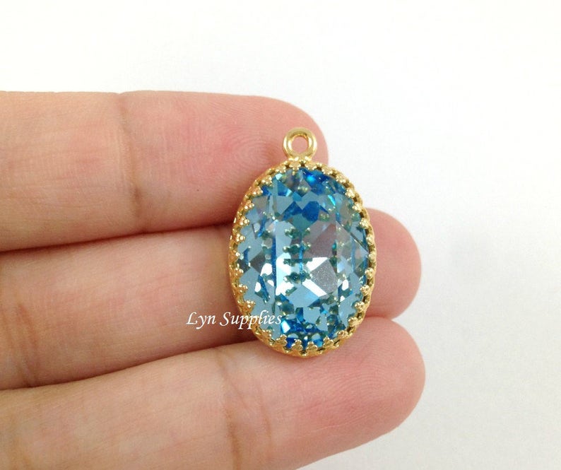 May include: A gold-toned pendant with a large, oval-shaped, light blue crystal. The crystal is faceted and has a gold-toned border.