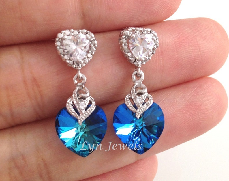 May include: A pair of silver heart-shaped earrings with a dangling blue crystal heart. The top heart is encrusted with clear rhinestones.