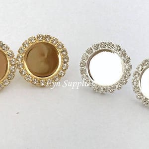 May include: Two pairs of round, gold and silver earring settings with clear rhinestones around the edge. The settings are designed to hold a round, flat, blank cabochon.