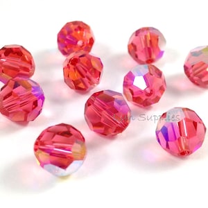 May include: A group of ten pink iridescent glass beads. The beads are round and have a faceted design.