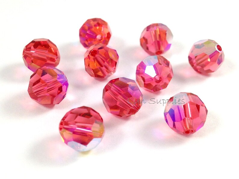 May include: A group of ten pink iridescent glass beads. The beads are round and have a faceted design.
