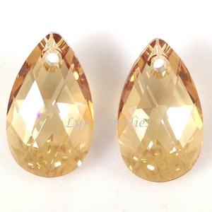 May include: Two teardrop-shaped crystal beads with a hole at the top for stringing. The beads are a light amber colour and have a faceted design.