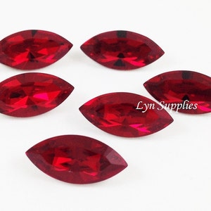 Könnte beinhalten: Sechs rote, marquiseförmige Strasssteine, jeder mit einer facettierten Oberfläche, sind auf einem weißen Hintergrund angeordnet. Die Strasssteine sind etwa 2,5 cm lang.
