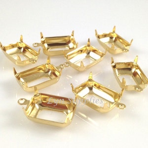May include: A collection of gold-colored, rectangular jewelry settings. Each setting has four prongs and small loops on the sides. The settings are designed to hold gemstones or other decorative elements.
