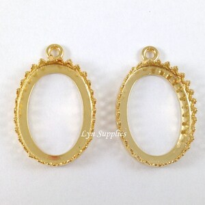 May include: Two gold oval pendant bezel settings with a beaded edge. The bezels have a loop at the top for attaching a chain or cord.