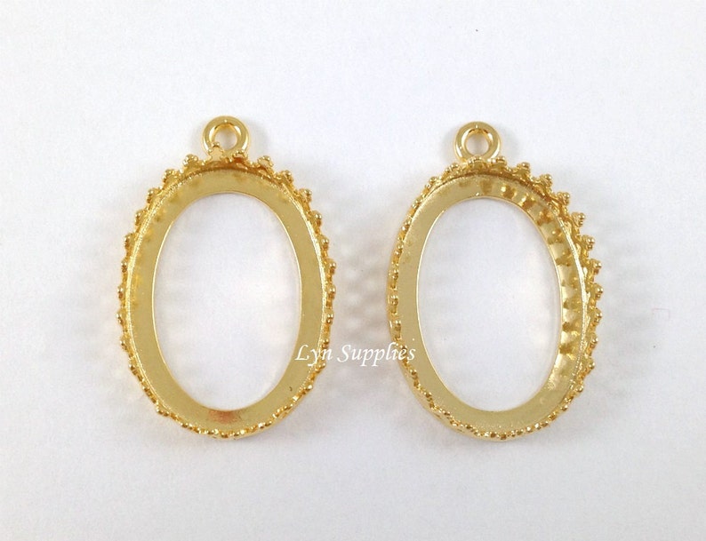 May include: Two gold oval pendant bezel settings with a beaded edge. The bezels have a loop at the top for attaching a chain or cord.
