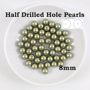 May include: A pile of 8mm half drilled hole green pearls on a white plate. The pearls have a slight iridescent sheen.