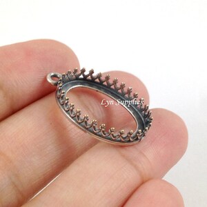 May include: Silver oval pendant bezel with a crown design. The bezel is open on the back and has a loop for attaching a chain.