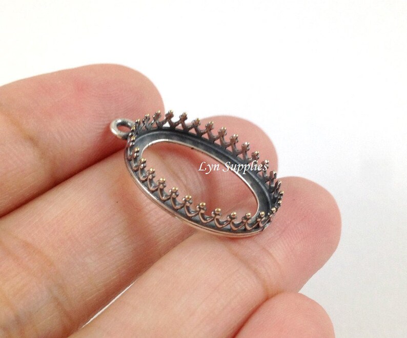 May include: Silver oval pendant bezel with a crown design. The bezel is open on the back and has a loop for attaching a chain.