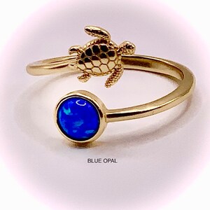 May include: Gold ring with a blue opal stone and a small turtle charm. The ring is open and adjustable.
