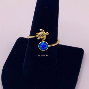 May include: Gold ring with a blue opal stone and a small turtle design. "BLUE OPAL" is written below the ring.