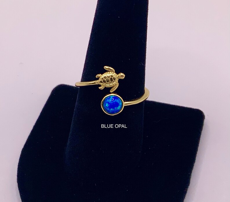 May include: Gold ring with a blue opal stone and a small turtle design. "BLUE OPAL" is written below the ring.