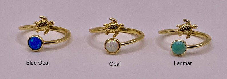 May include: Three gold rings with a turtle charm and a gemstone. The rings are available with a blue opal, white opal, and a light blue larimar stone.