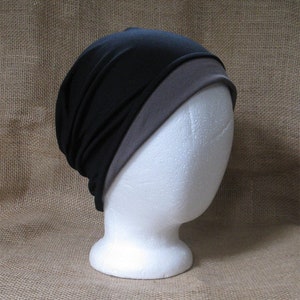 May include: A black and gray beanie hat made of soft fabric. The hat is folded over at the top and has a simple design.