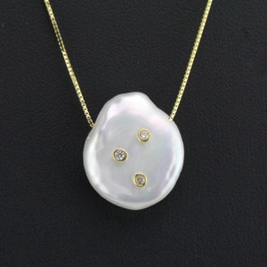 Könnte beinhalten: Eine Halskette mit einem Anhänger aus einer weißen Barockperle und drei kleinen, klaren Diamanten, die in Gold gefasst sind.