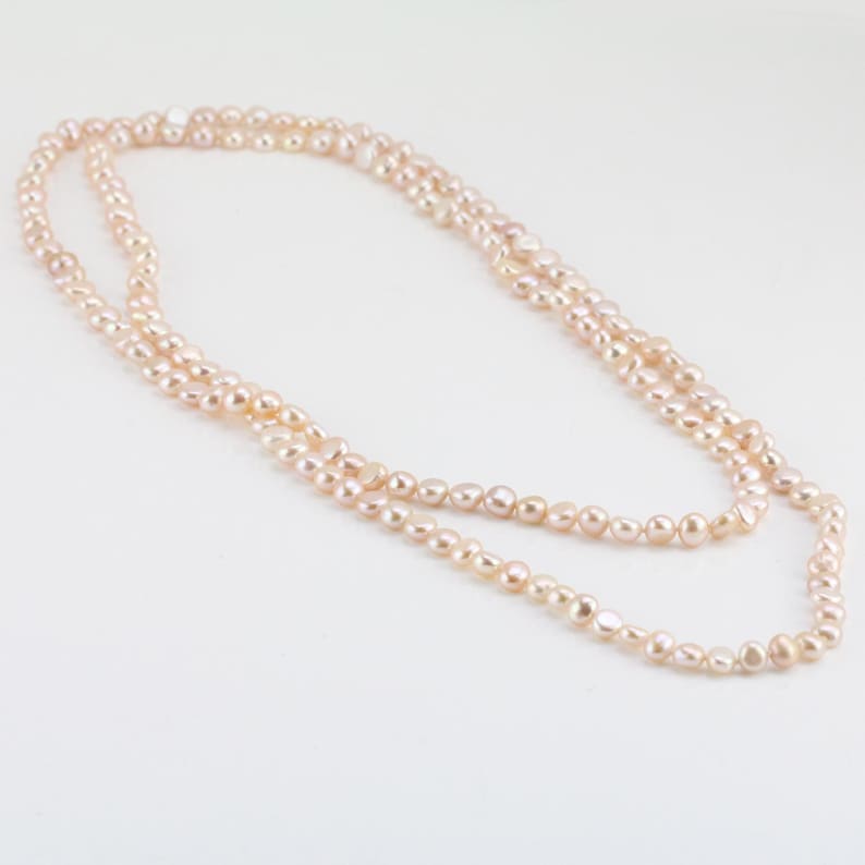 May include: A long, delicate necklace made of pale pink freshwater pearls. The pearls are strung on a thin silver chain and are arranged in a simple, elegant design.