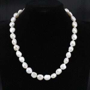 May include: A white pearl necklace with large, irregular shaped pearls. The necklace is on a black velvet background.